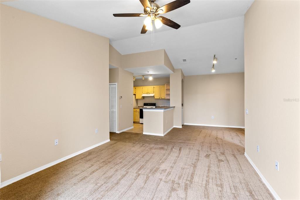 A living room with beige carpet and walls leads to an open kitchen with yellow cabinets — 1440 LAKE SHADOW CIRCLE UNIT 8305, MAITLAND, FL