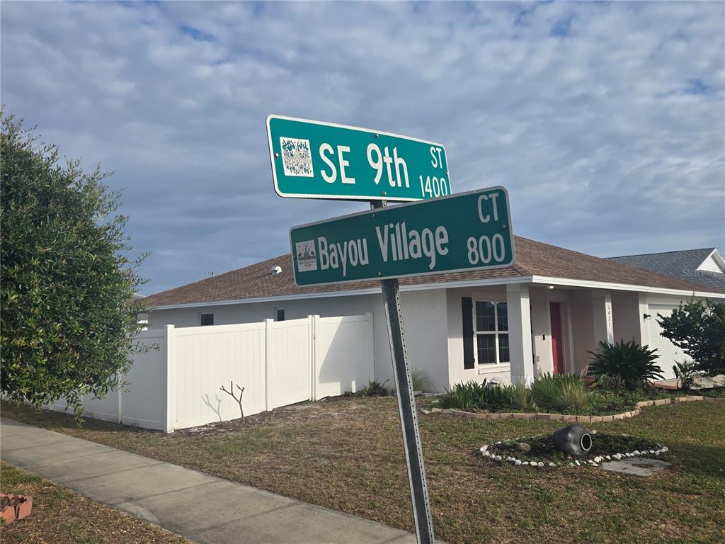 A street sign for SE 9th St and Bayou Village Ct stands before a suburban house — 1421 9TH STREET SE, RUSKIN, FL