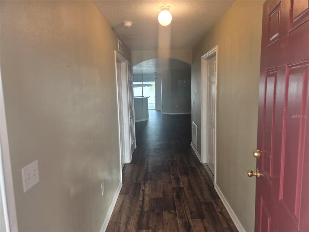 A hallway with wood-look flooring leads from a red front door to an open living area — 1421 9TH STREET SE, RUSKIN, FL