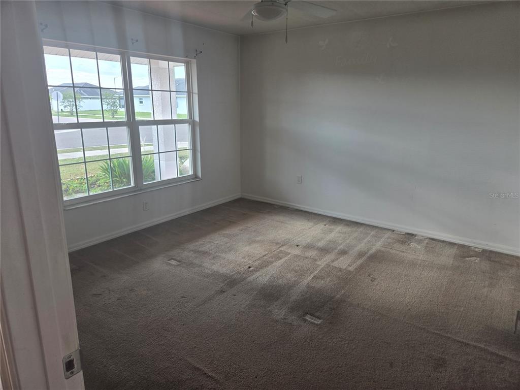 An empty bedroom features beige carpet, white walls, and a large window overlooking a street — 1421 9TH STREET SE, RUSKIN, FL