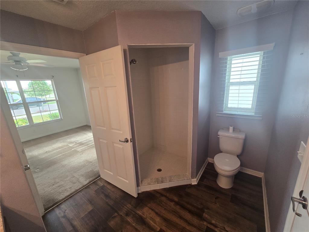 A bathroom features a corner shower, a toilet, and wood-look flooring, with an adjacent bedroom — 1421 9TH STREET SE, RUSKIN, FL