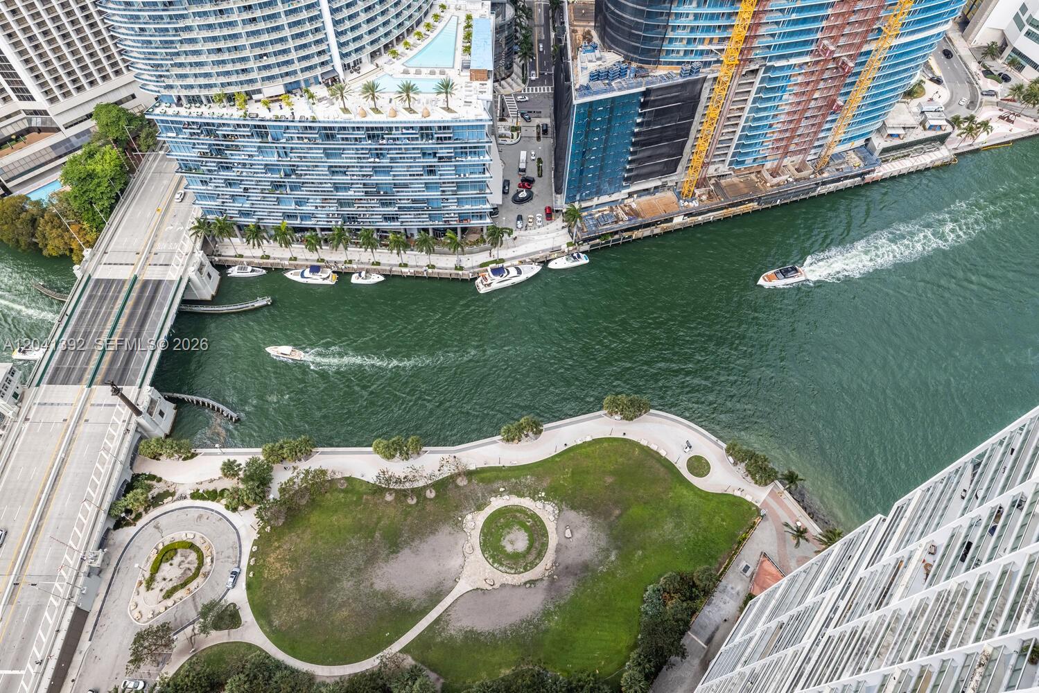 An aerial view shows a waterfront park, a bridge, and high-rise buildings along a river — 475 BRICKELL AVE # 4715, Miami FL 33131, MIAMI, FL