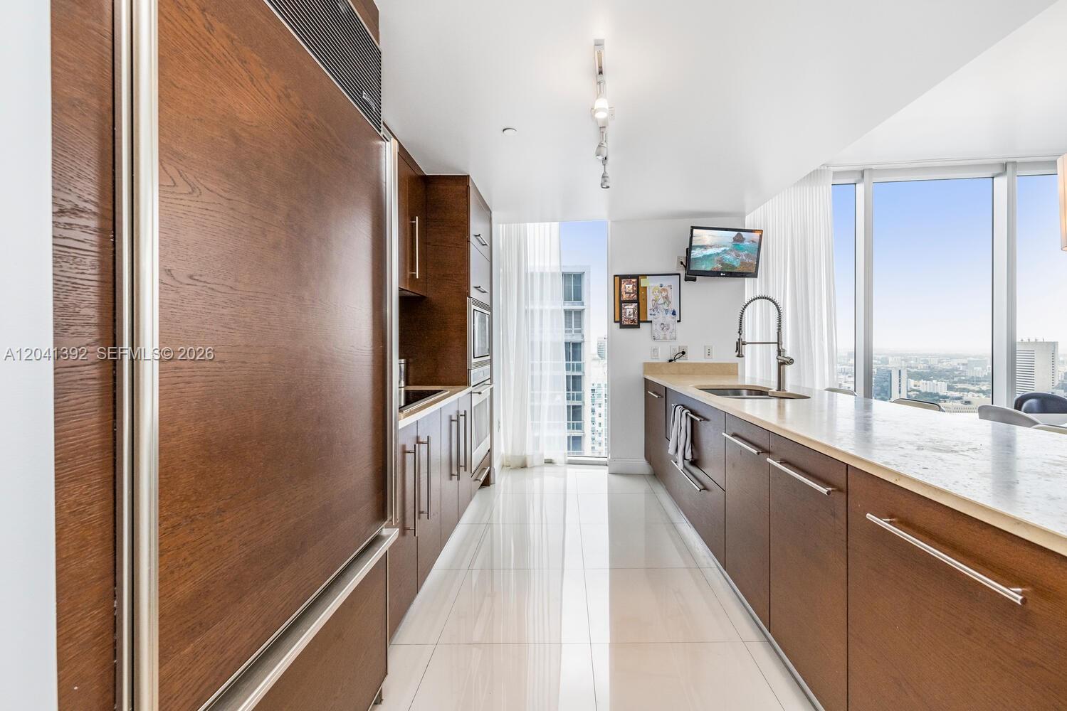 A modern kitchen features dark wood cabinetry, white countertops, and floor-to-ceiling windows with city views — 475 BRICKELL AVE # 4715, Miami FL 33131, MIAMI, FL