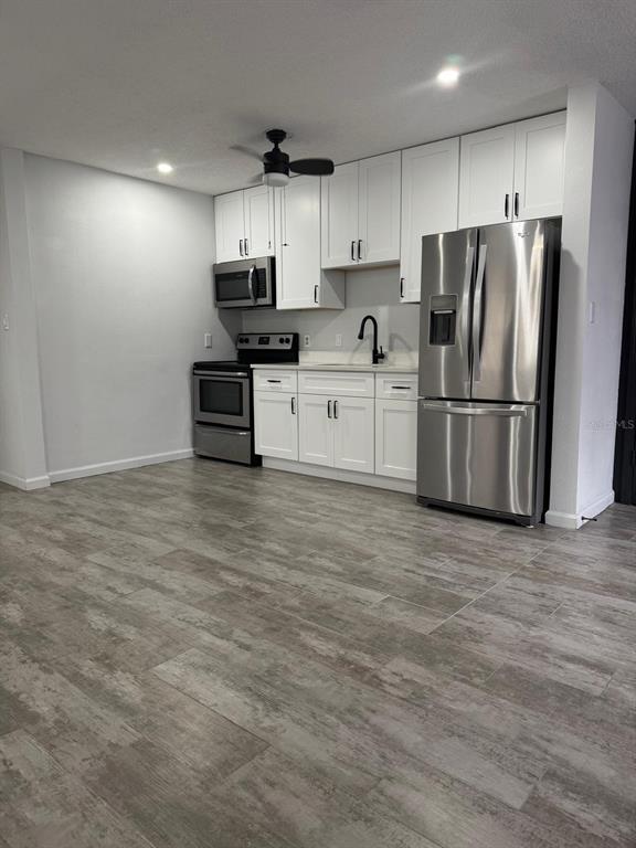 An open-concept living area features light wood-look tile flooring, white walls, and a dark door — 1905 ROSLYN AVENUE, BRADENTON, FL