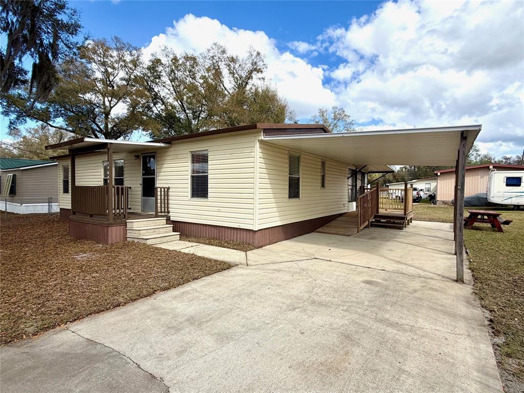 A single-story mobile home with beige siding, a front porch, and a concrete carport — 14645 SE 47TH AVENUE, SUMMERFIELD, FL