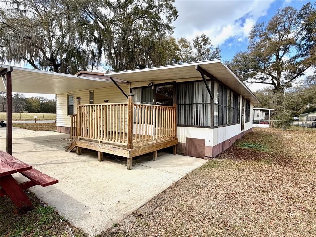 A mobile home exterior features a wooden deck, a concrete patio, and a metal carport — 14645 SE 47TH AVENUE, SUMMERFIELD, FL