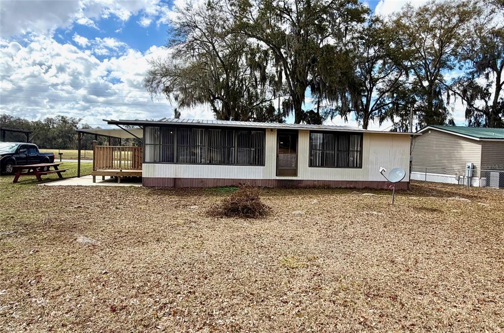 A single-story mobile home with a screened-in porch and a wooden deck sits outdoors — 14645 SE 47TH AVENUE, SUMMERFIELD, FL