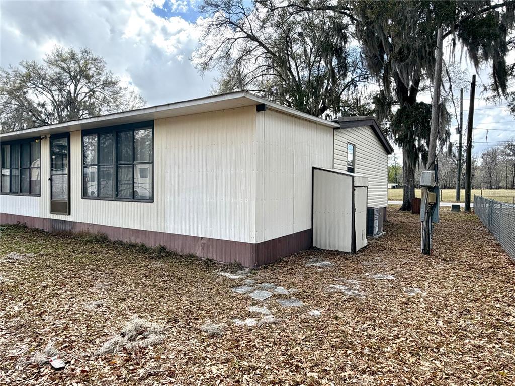 The exterior of a mobile home features light-colored metal siding and a small attached shed — 14645 SE 47TH AVENUE, SUMMERFIELD, FL