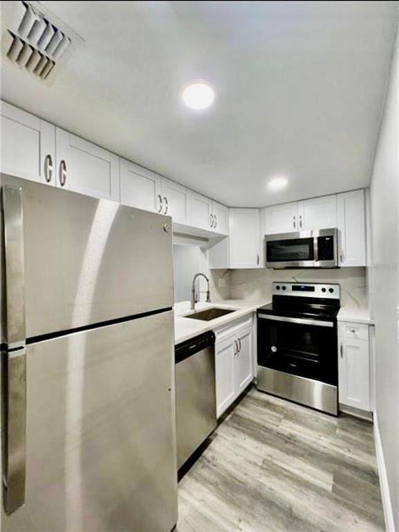 A kitchen features stainless steel appliances, white cabinetry, and light wood-look flooring — 7108 WATERSIDE DRIVE UNIT 103, TAMPA, FL