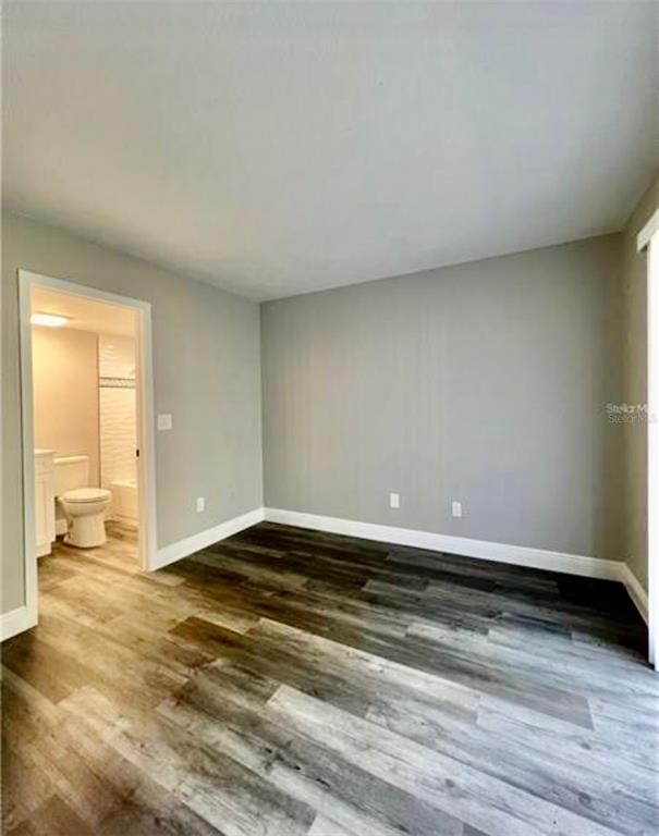 A bedroom with gray walls, wood-look flooring, and an attached bathroom with a toilet — 7108 WATERSIDE DRIVE UNIT 103, TAMPA, FL