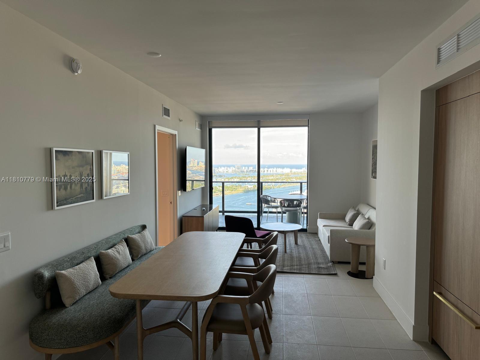 A modern living and dining area features a balcony with water and city skyline views — 159 NE 6TH ST # 4215, Miami FL 33132, MIAMI, FL