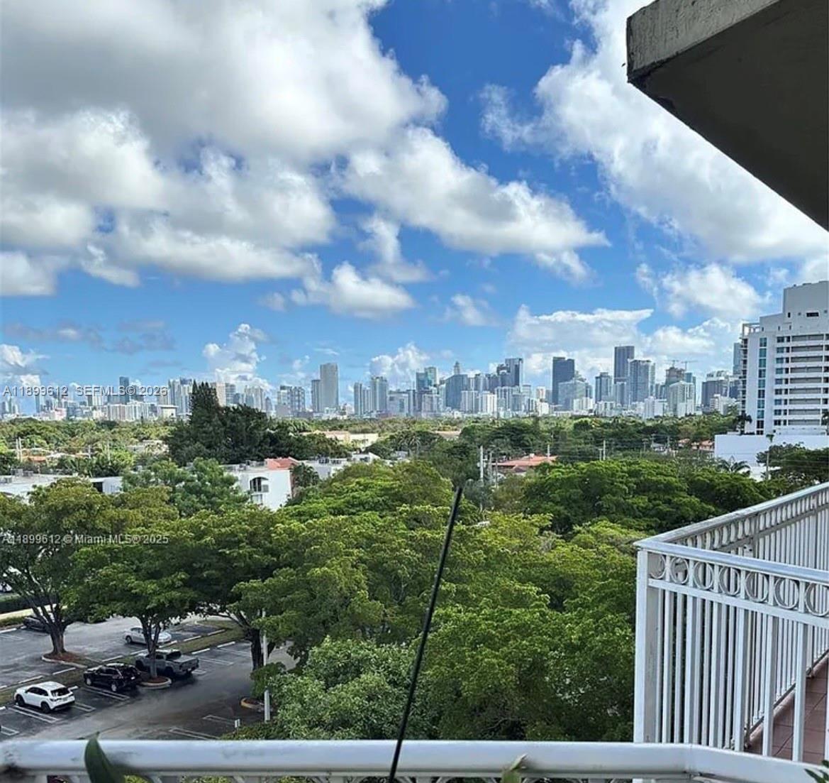 A balcony view overlooks a lush green canopy with a distant city skyline under clouds — 1650 Coral Way # 808, Miami FL 33145, MIAMI, FL