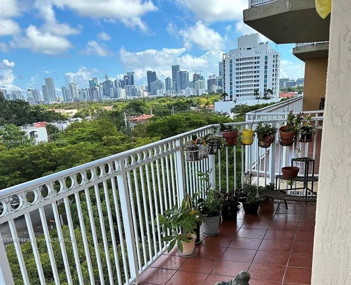 A balcony with potted plants overlooks a lush green area and a city skyline — 1650 Coral Way # 808, Miami FL 33145, MIAMI, FL