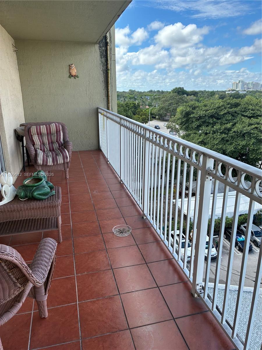 A balcony with reddish-brown tile flooring, wicker furniture, and a white metal railing overlooking trees — 1650 Coral Way # 808, Miami FL 33145, MIAMI, FL