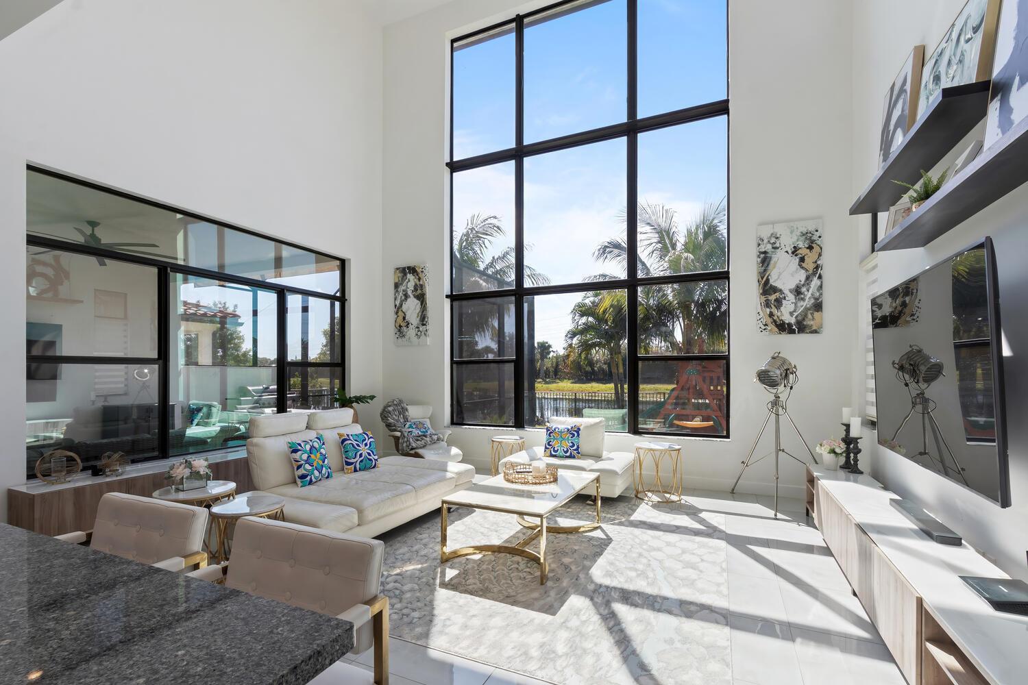 A bright living room features high ceilings, floor-to-ceiling windows, white furniture, and tile flooring — 8451 Grand Prix Lane, Boynton Beach FL 33472, BOYNTON BEACH, FL