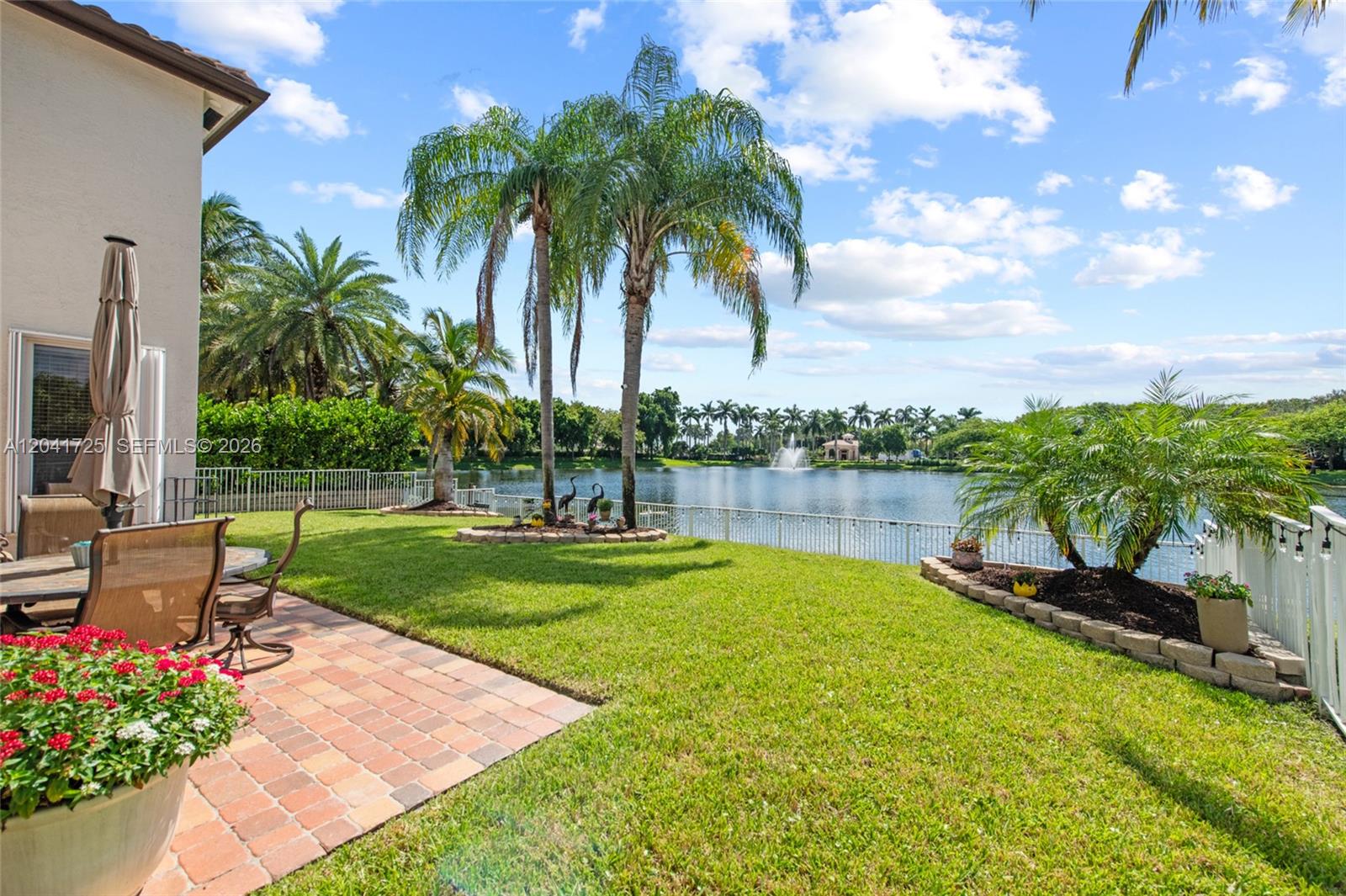 A backyard patio with a dining set overlooks a lake with a fountain and palm trees — 16230 SW 21st St, Miramar FL 33027, MIRAMAR, FL