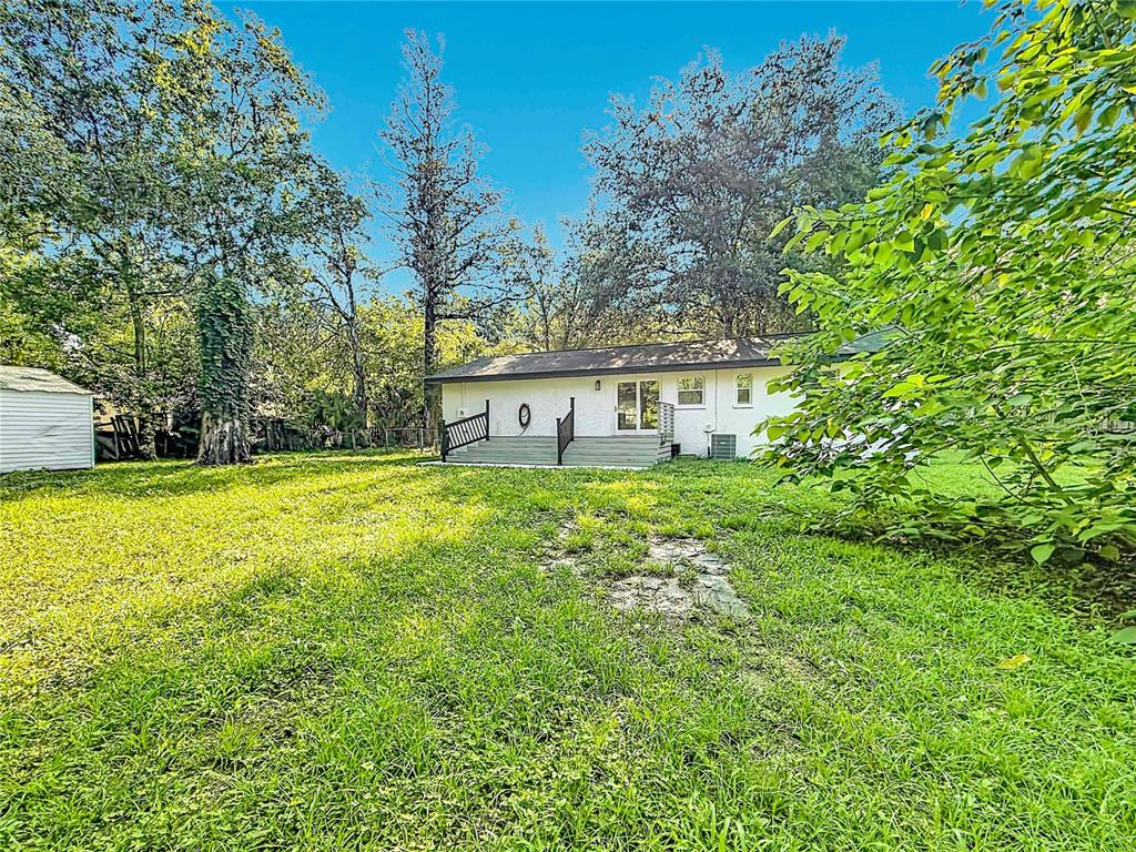 A white house with a wooden deck sits in a large, grassy backyard with trees — 11572 SE 60TH AVENUE, BELLEVIEW, FL