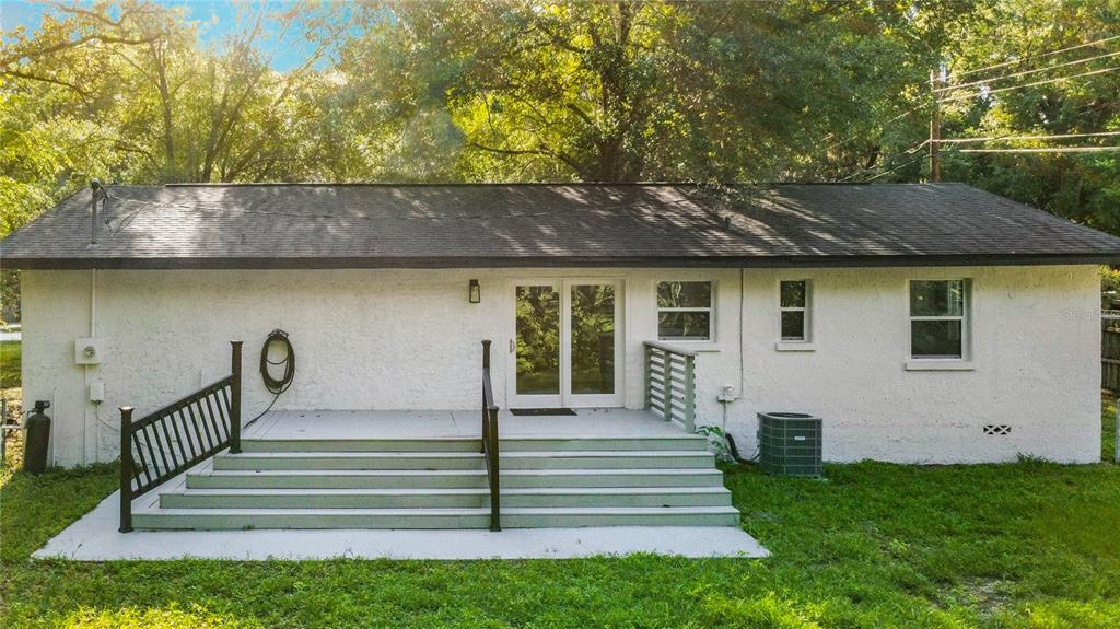 The exterior of a white, single-story house features a wooden deck with stairs and railings — 11572 SE 60TH AVENUE, BELLEVIEW, FL