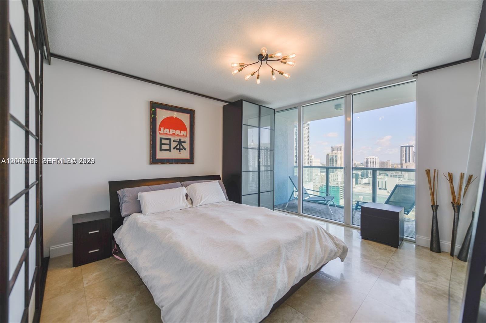 A modern bedroom features a bed, dark furniture, a Japanese poster, and a city balcony view — 31 SE 5th St # 3002, Miami FL 33131, MIAMI, FL