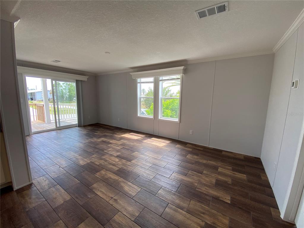 An empty living room features wood-look tile flooring, light gray walls, and a sliding glass door — 538 FLEETWOOD STREET, NORTH PORT, FL