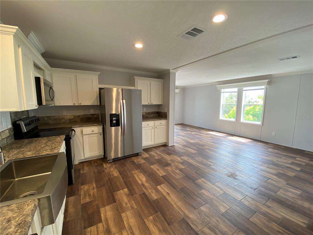 A kitchen with white cabinets, stainless steel appliances, and wood-look flooring opens to a living area — 538 FLEETWOOD STREET, NORTH PORT, FL