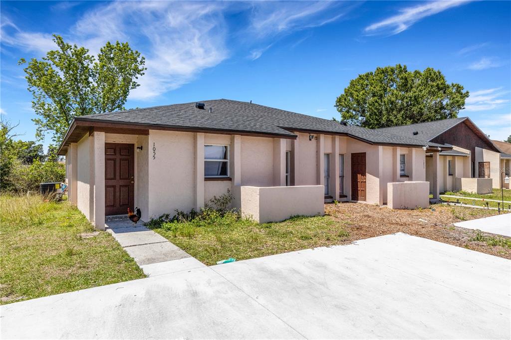 A single-story duplex with a concrete driveway, tan stucco exterior, and a rooster on the walkway — 1053 / 1055 CAPTIVA POINT, LAKELAND, FL