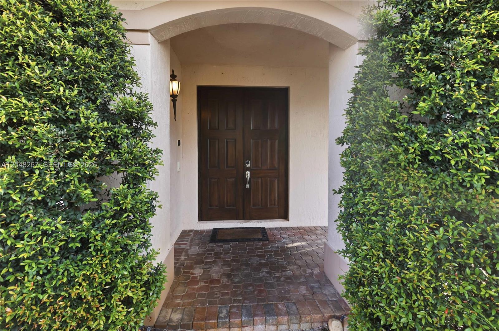 A dark wood double front door is framed by two large bushes and brick flooring — 1419 Crossbill Ct # 1419, Weston FL 33327, WESTON, FL
