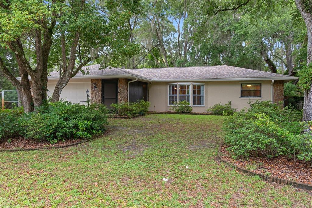 A single-story ranch-style house with a stone facade, a garage, and large shade trees — 5931 N BROOKGREEN DRIVE, CRYSTAL RIVER, FL