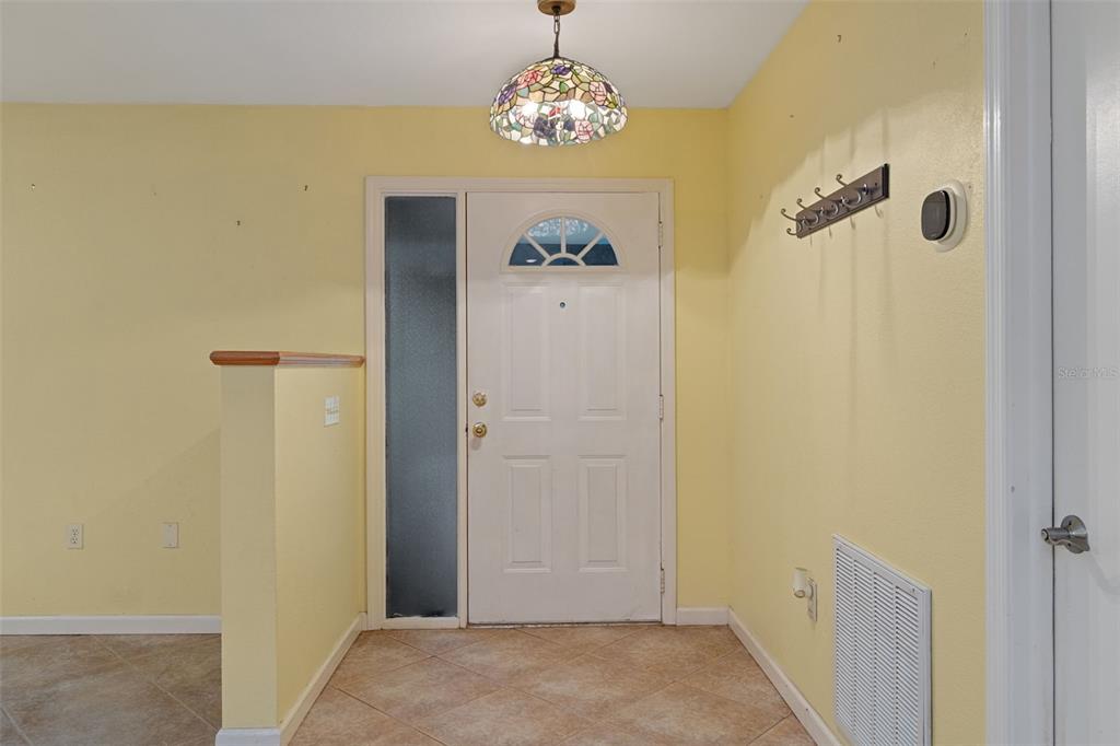 An entryway with yellow walls, tile flooring, a stained-glass light fixture, and a white door — 5931 N BROOKGREEN DRIVE, CRYSTAL RIVER, FL