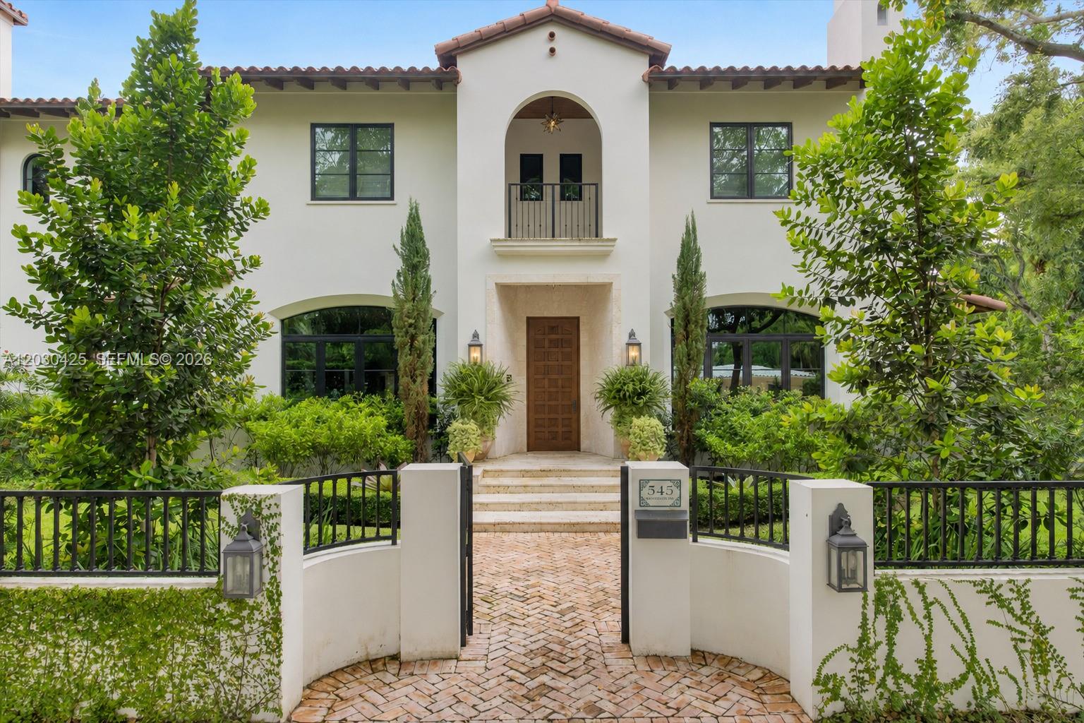 A two-story Mediterranean-style house features a gated brick walkway, arched balcony, and lush landscaping — 545 San Antonio Ave, Coral Gables FL 33146, CORAL GABLES, FL