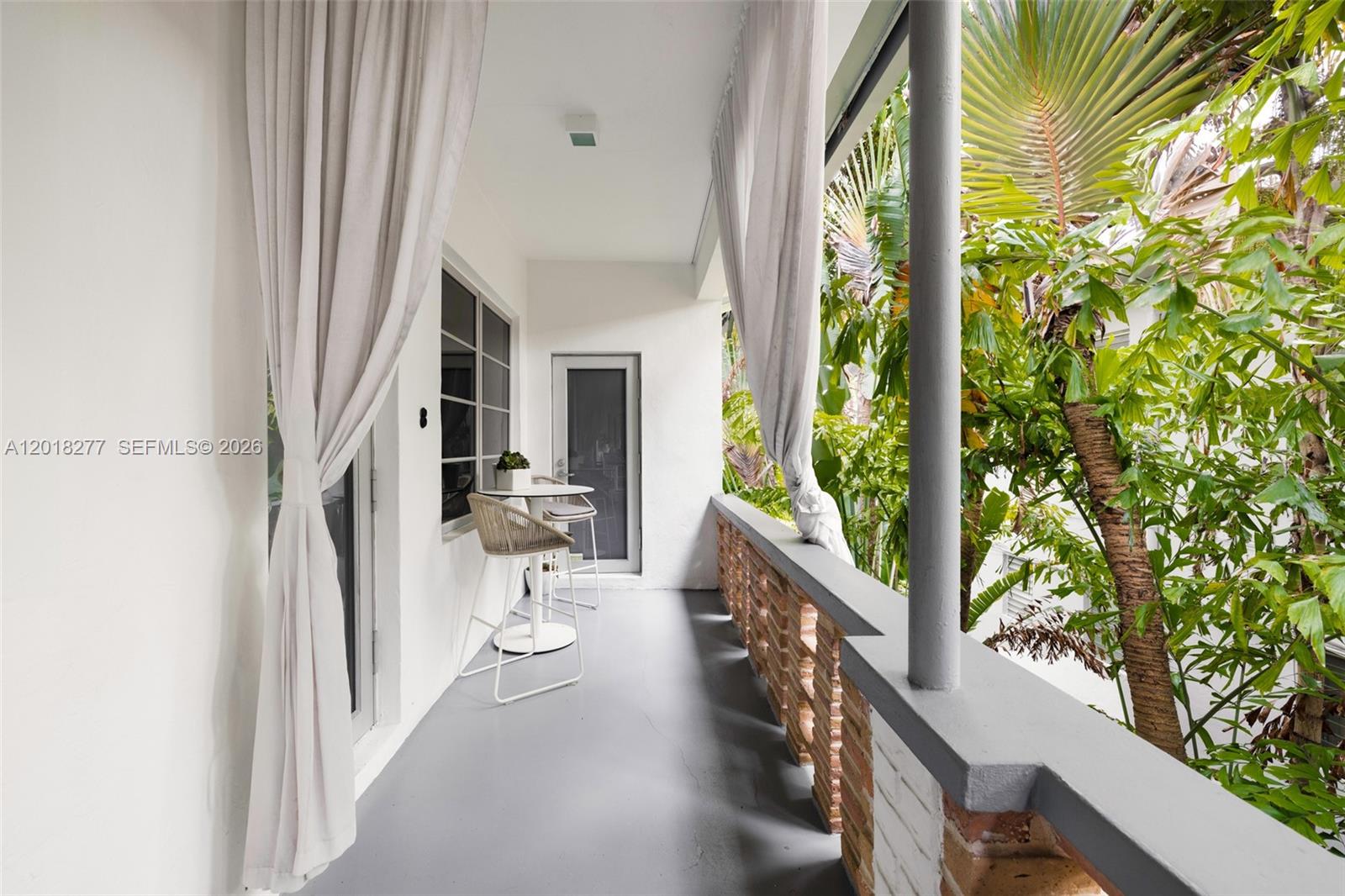 A balcony features a small table with two chairs, white curtains, and a brick railing — 1551 Lenox Ave # 8, Miami Beach FL 33139, MIAMI BEACH, FL