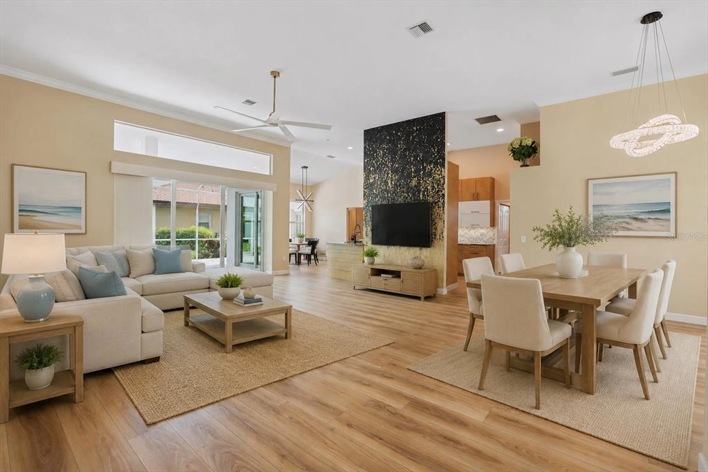 An open-concept living and dining area features light wood floors, a black accent wall, and neutral furniture — 567 LAKE OF THE WOODS DRIVE, VENICE, FL