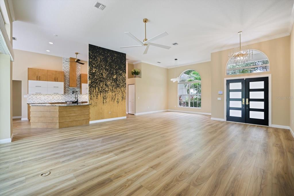 An open-concept living area features light wood flooring, a black-and-gold accent wall, and a kitchen — 567 LAKE OF THE WOODS DRIVE, VENICE, FL