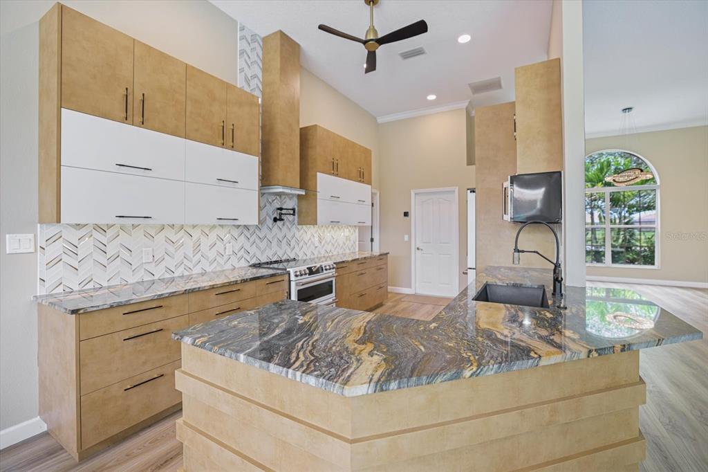 A kitchen features light wood cabinets, white upper doors, patterned backsplash, and dark stone countertops — 567 LAKE OF THE WOODS DRIVE, VENICE, FL