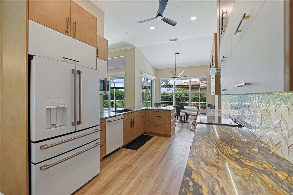 A modern kitchen features wood cabinets, white appliances, patterned countertops, and a view of the outdoors — 567 LAKE OF THE WOODS DRIVE, VENICE, FL