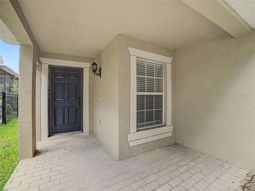A covered entryway features a dark blue front door, a window, and light-colored paver flooring — 5828 WRENWATER DRIVE, LITHIA, FL