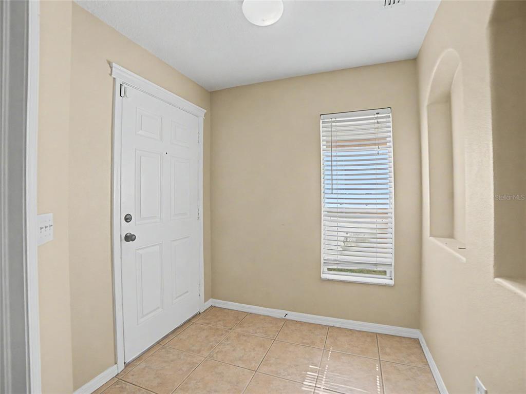 An entryway with a white door, tiled floor, beige walls, and a window with blinds — 5828 WRENWATER DRIVE, LITHIA, FL