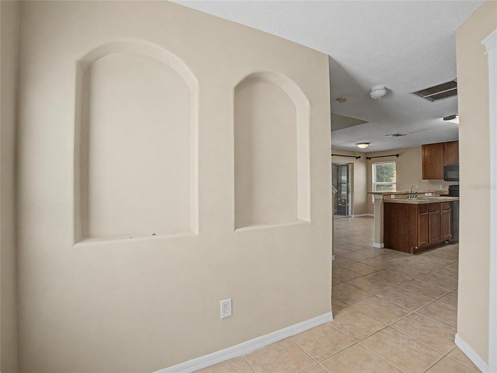 A beige wall features two arched niches, leading into a kitchen with tile flooring — 5828 WRENWATER DRIVE, LITHIA, FL