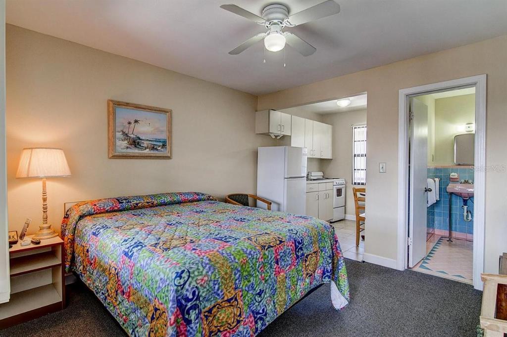 A bedroom with a patterned quilt, a ceiling fan, a small kitchenette, and an attached bathroom — 653 MANDALAY AVENUE, CLEARWATER, FL