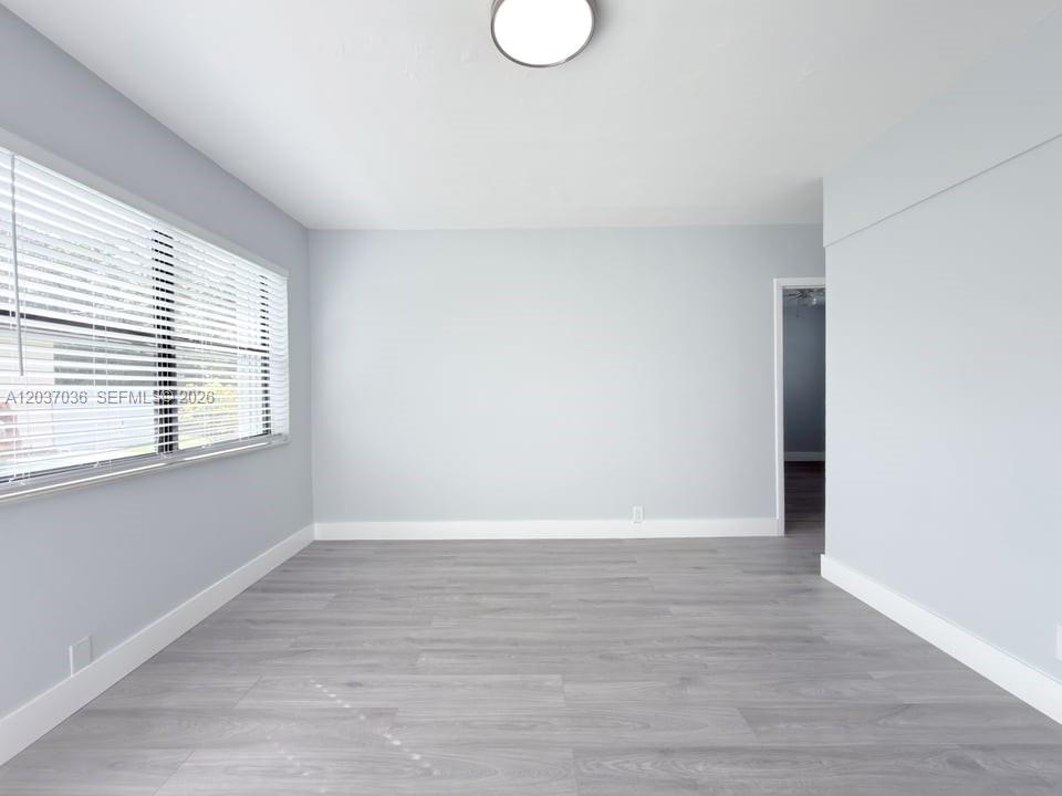 An empty room features light gray walls, wood-look flooring, and a window with white blinds — 1010 Opa Locka Blvd # 3, Opa-Locka FL 33054, OPA-LOCKA, FL