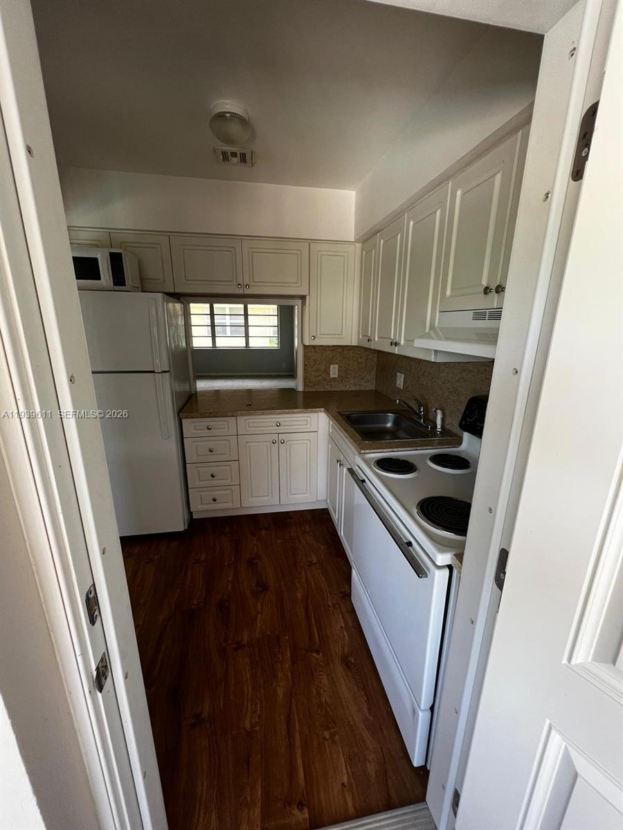 A galley kitchen features white cabinets, granite countertops, and wood-look flooring — 2701 NE 1st St # 203, Pompano Beach FL 33062, POMPANO BEACH, FL