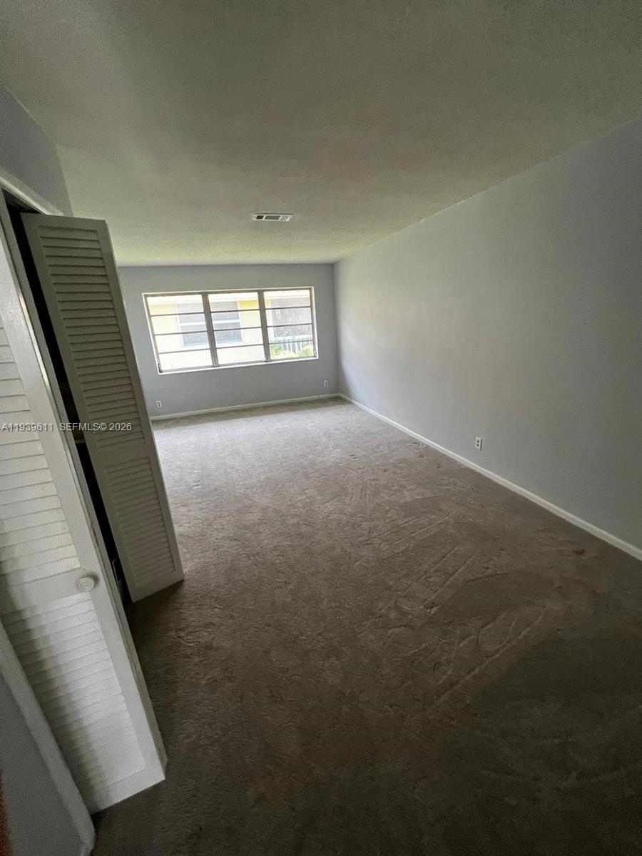 An empty room features light gray walls, beige carpeting, and a white louvered closet door — 2701 NE 1st St # 203, Pompano Beach FL 33062, POMPANO BEACH, FL