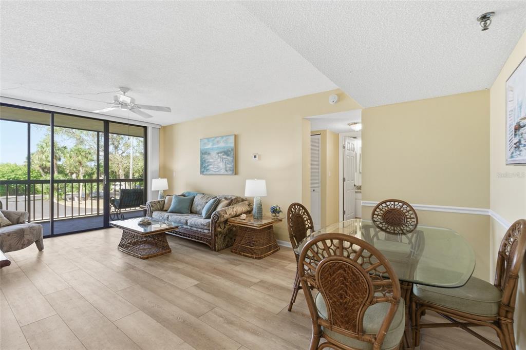 A living and dining area with light wood floors, wicker furniture, and a glass balcony door — 3006 CARING WAY UNIT 224, PORT CHARLOTTE, FL