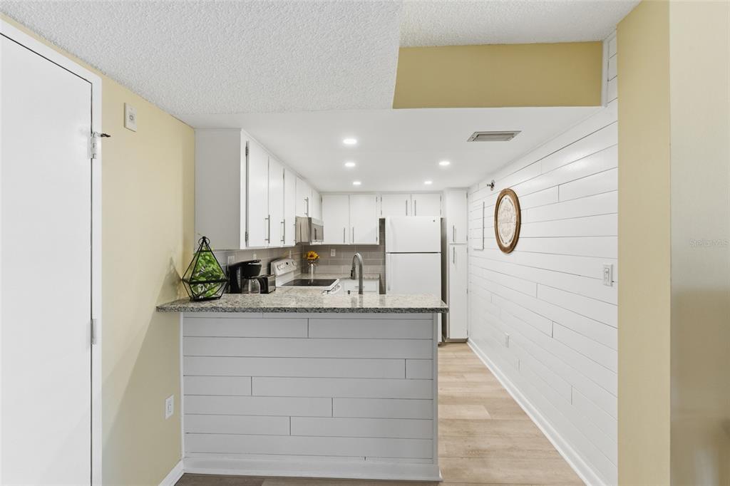 A kitchen features white cabinets, granite countertops, a breakfast bar, and white shiplap wall paneling — 3006 CARING WAY UNIT 224, PORT CHARLOTTE, FL
