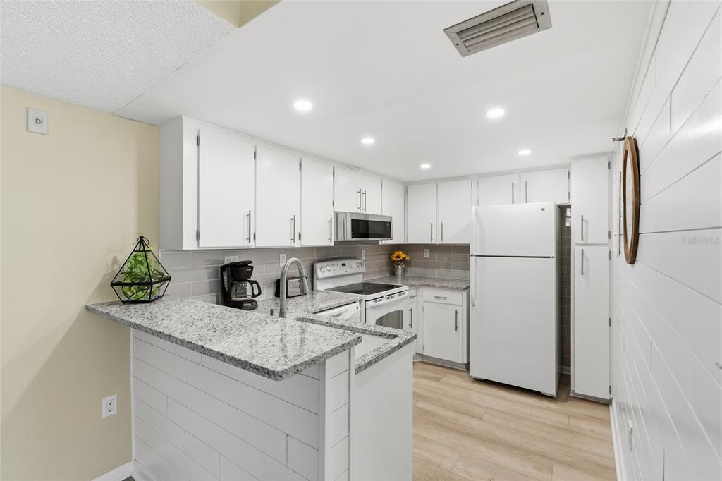 A kitchen features white cabinets, granite countertops, a white refrigerator, and a breakfast bar — 3006 CARING WAY UNIT 224, PORT CHARLOTTE, FL