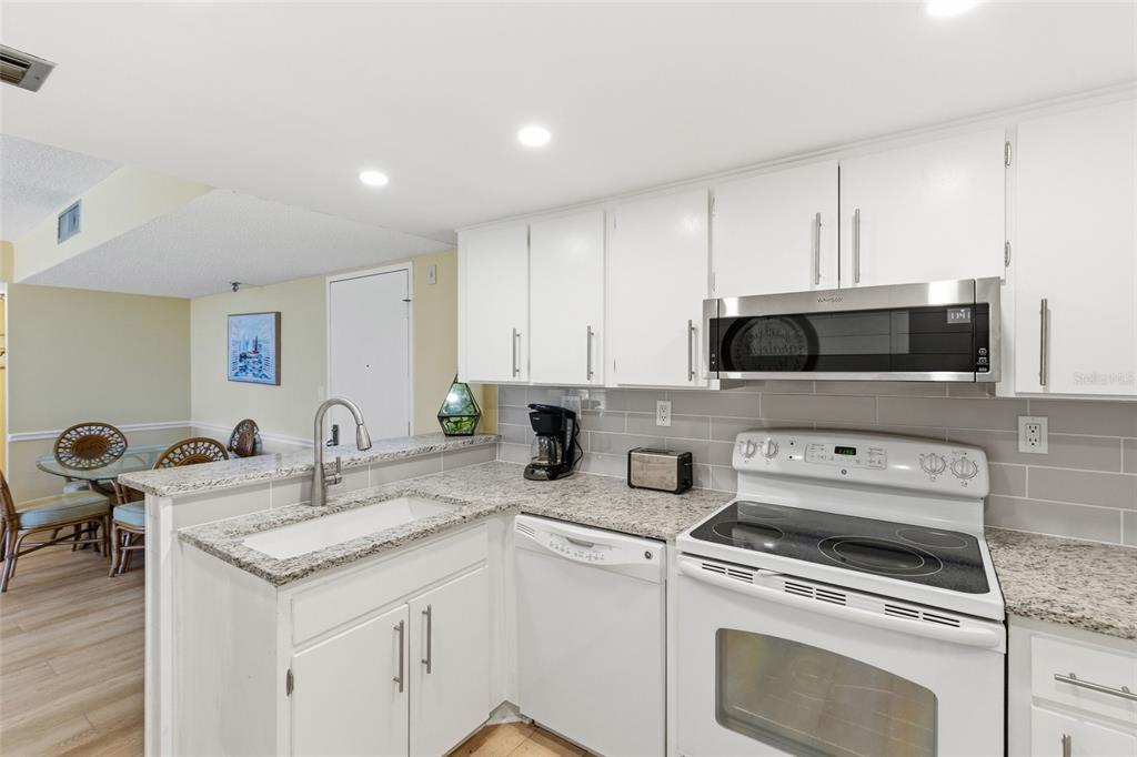 A kitchen with white cabinets, granite countertops, a stainless steel microwave, and a white stove — 3006 CARING WAY UNIT 224, PORT CHARLOTTE, FL