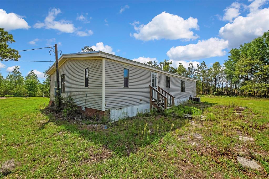 A single-story manufactured home with light gray siding sits on a grassy, wooded lot — 4512 N TIMBERWOOD POINT, CRYSTAL RIVER, FL