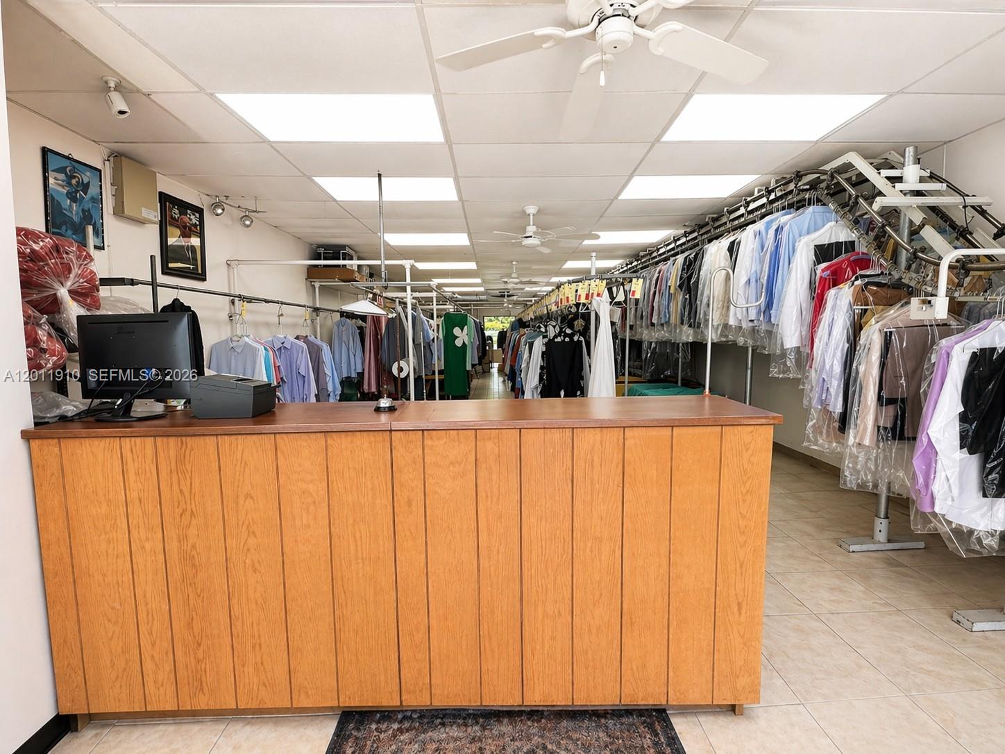 A dry cleaning shop interior features a wooden service counter and rows of hanging clothes — 10114 S Military Trl, Boynton Beach FL 33436, BOYNTON BEACH, FL