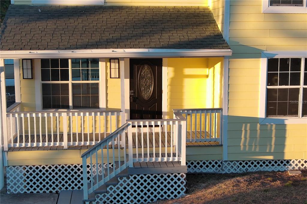 A yellow house features a front porch with white railings, lattice skirting, and a dark door — 3906 28TH STREET SW, LEHIGH ACRES, FL