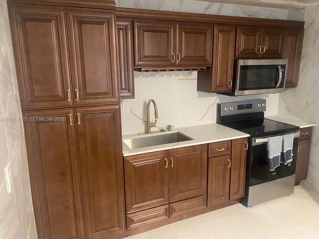 A kitchen features dark wood cabinets, stainless steel appliances, and white marble-patterned countertops and backsplash — 712 57th St, West Palm Beach FL 33407, WEST PALM BEACH, FL